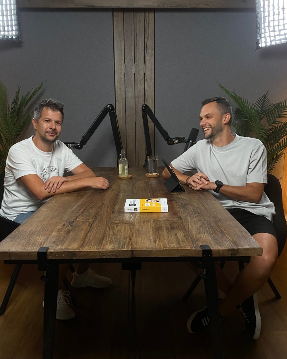 Oťas s hostem u stolu v podcastovém studiu, oba se smějí.